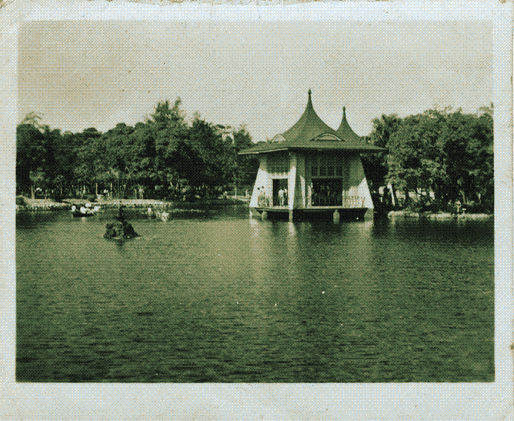 A building with a slanted curved roof at the edge of a lake, surrounded by trees
